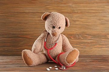 Cute teddy bear with stethoscope on wooden background