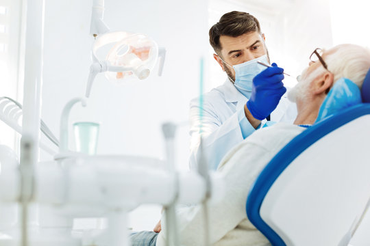 Be calm. Concentrated skilled dental surgeon using specific tools while curing patients teeth