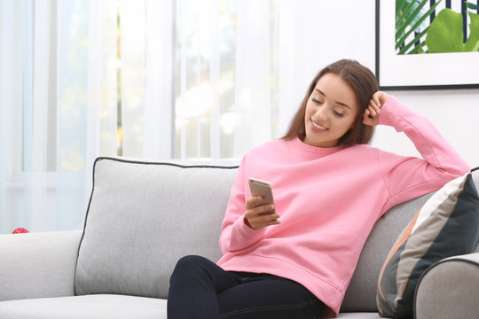 Young woman with mobile phone on sofa at home