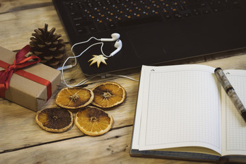 Naklejka na ściany i meble Workplace. On a wooden table, a laptop, a cup of coffee, headphones, a notebook, a pen. Gift, fir cone and sliced ​​oranges