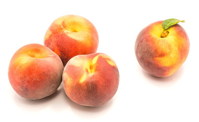 Group of four whole peaches, one with green leaf, isolated on white background.
