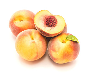 Folded peaches, one with green leaf and one sliced half with a stone, isolated on white background.