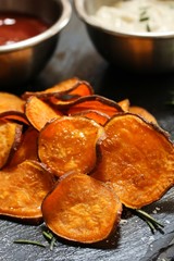 Homemade baked sweet potato chips with dips on dark moody background, selective focus