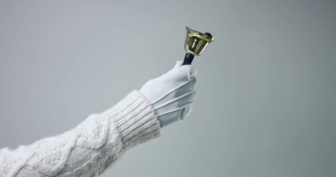 Hand in white leather glove and white cable sweater ringing a golden bell on white background