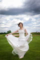 Attractive young bride in a modern white dress running on a green golf course . Concept of fashion modern bride