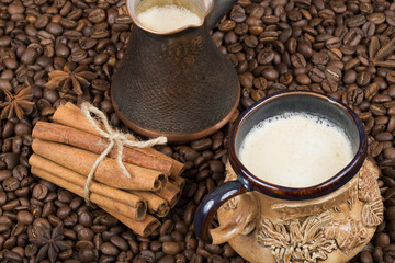 A cup of freshly brewed coffee, pot and cinnamon on coffee beans
