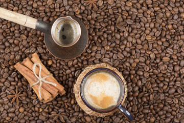 A cup of freshly brewed coffee, pot and cinnamon on coffee beans