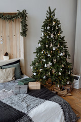 The bedroom decorated by Christmas. Cozy light interior: plaid, wooden bed. On a bed the packed gifts lie. In the room there is a New Year's fir-tree decorated with toys and garlands.