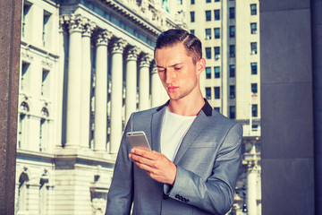 Fototapeta premium Eastern European Businessman working in New York, wearing gray fashionable blazer, standing by vintage office building, looking down, reading messages on cell phone. Instagram filtered effect..
