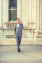 Eastern European Businessman working in New York. Wearing gray fashionable suit, leather shoes, hand put in pocket, a lawyer walking on hall way of vintage law office building, talking on cell phone..