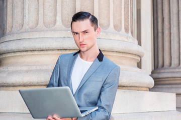 American Businessman working in New York. Dressing in gray fashionable blazer, white undershirt, a young lawyer standing by column, working on laptop computer, thinking. Filtered look with blue tint..