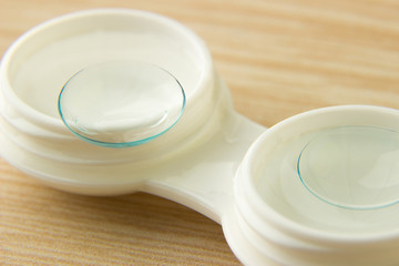 Contact lenses for the eyes and a white container with a solution on a wooden table