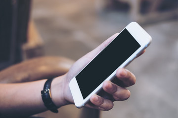 Mockup image of a woman's hand holding white mobile phone with blank black screen , concrete floor background