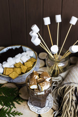 a cup of cocoa with marshmallow on a wooden table next to a rug and sweets