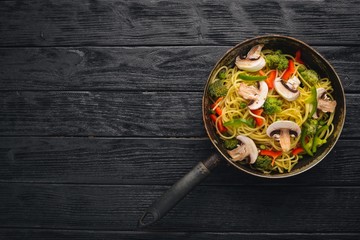 Noodles with vegetables in a frying pan. Asian Cuisine Pasta. Top view. Free space. On a wooden background.;