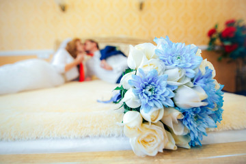 newlyweds lie on a bed in the foreground a wedding bouquet