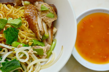 dry Chinese egg noodle topping duck meat and bean sprout on bowl with chili sauce cup