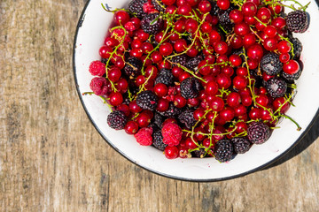 Fresh colorful berries in bowl on rustic wooden table