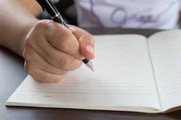 Closeup of woman's hand writing on paper book
