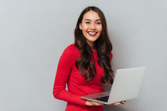 Happy brunette woman in red blouse holding laptop computer