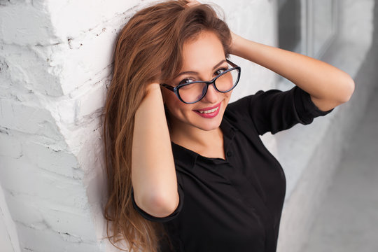 portrait of a beautiful girl close-up in the glasses smiles against the background of a white wall