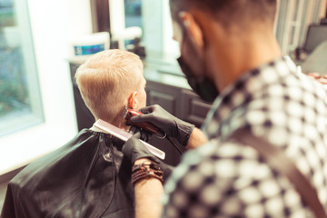 Handsome blonde man having his hair cut by hairdresser at the retro barbershop
