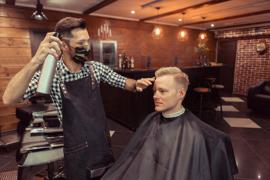 Handsome hairdresser cutting hair of male client. Men hairstylist serving client at vintage barber shop.