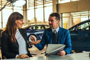 Fototapeta premium Young pretty woman receiving the keys of her new car.
