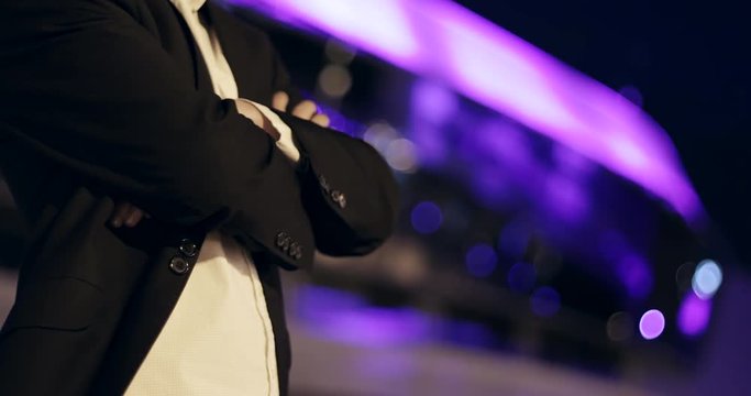 A man in a suit with a jacket and a white shirt in the city at night.