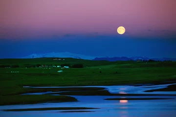 Reise nach Island. Schöne isländische Abendlandschaft mit grünen Feldern, Bergen, Himmel und Mond. © vitaliymateha
