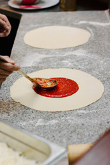 Chief putting tomato sauce on the round of pizza dough.