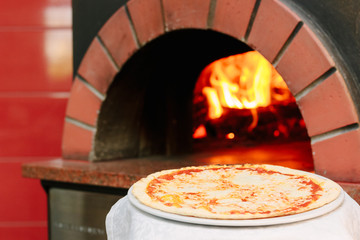 Fresh hot italian pizza with the traditional pizza oven with flame as background.