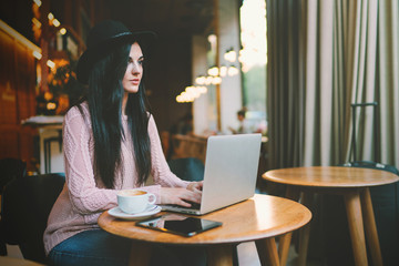 Professional journalist typing new story on a portable computer while sitting in a coffee shop. Successful beauty blogger writing emails on a laptop while sitting with a cup of coffee in a cafe.