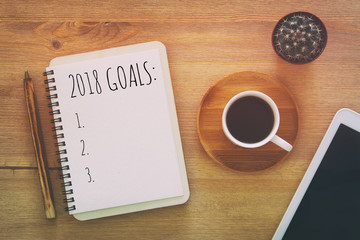 Top view 2018 goals list with notebook, cup of coffee on wooden desk.