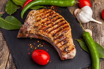 Grilled pork steak on the bone with seasonings and grilled tomatoes on a black background. Top view