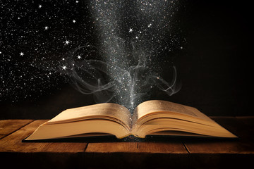 Obraz premium image of open antique book on wooden table with glitter overlay.