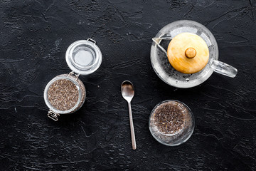 Brew chia seeds. Jar with seeds, scoop, bowl, tea pot with hot water. Black background top view
