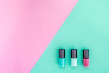 Cosmetics on colorful background. Mint and cherry nail polish on pink and mint background top view copyspace