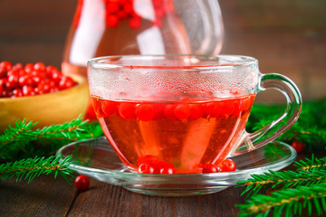 Hot tea from cranberries in a glass cup surrounded by fir branches on a wooden table.
