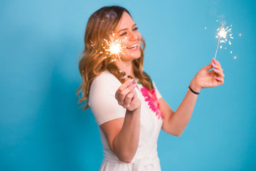 Happy woman having fun with a sparkler on blue background with copyspace