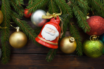 Green living spruce branches on a dark wooden background. New Year background with multi-colored balloons and bells in the idea of Santa Claus. Top view