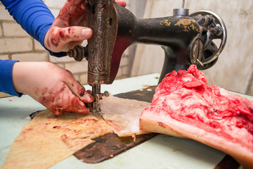 a woman sews from bloody skin and meat on an old retro sewing machine. Animal protection