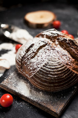 freshly baked bread, flour and tomatoes on a wooden board on a table