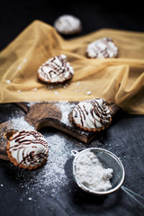small chocolate cakes with different stuffings, sprinkled with chocolate topping, sprinkled with powdered sugar on a wooden board, on a golden napkin on a dark background