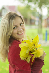 Naklejka premium Beautiful pregnant woman in a red coat holds yellow leaves.