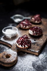 small chocolate cakes with different stuffings, sprinkled with berry topping, sprinkled with powdered sugar on a wooden board on a dark background