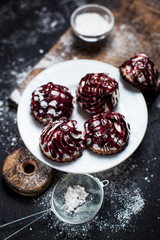 small desserts with different stuffings, sprinkled with berry topping, sprinkled with powdered sugar on a white plate on a wooden board on a dark background