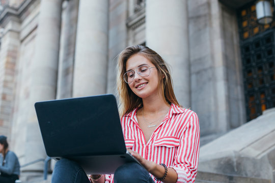 Portrait of fashion student or graphic designer freelancer, woman works on laptop in summer, remotely finishing work project, sits on steps of building in city, happy and smiling, confident in future