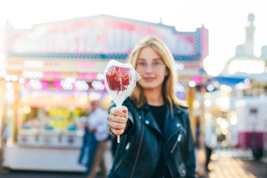 Attractive and trendy young millennial teenager or hipster woman in fashionable latest fashion outfit, leather jacket and vintage glasses poses with sweet treat, candy caramel coated apple
