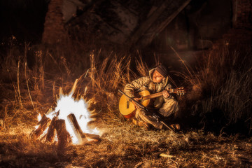 Armed rebel resting by the fire and playing the guitar